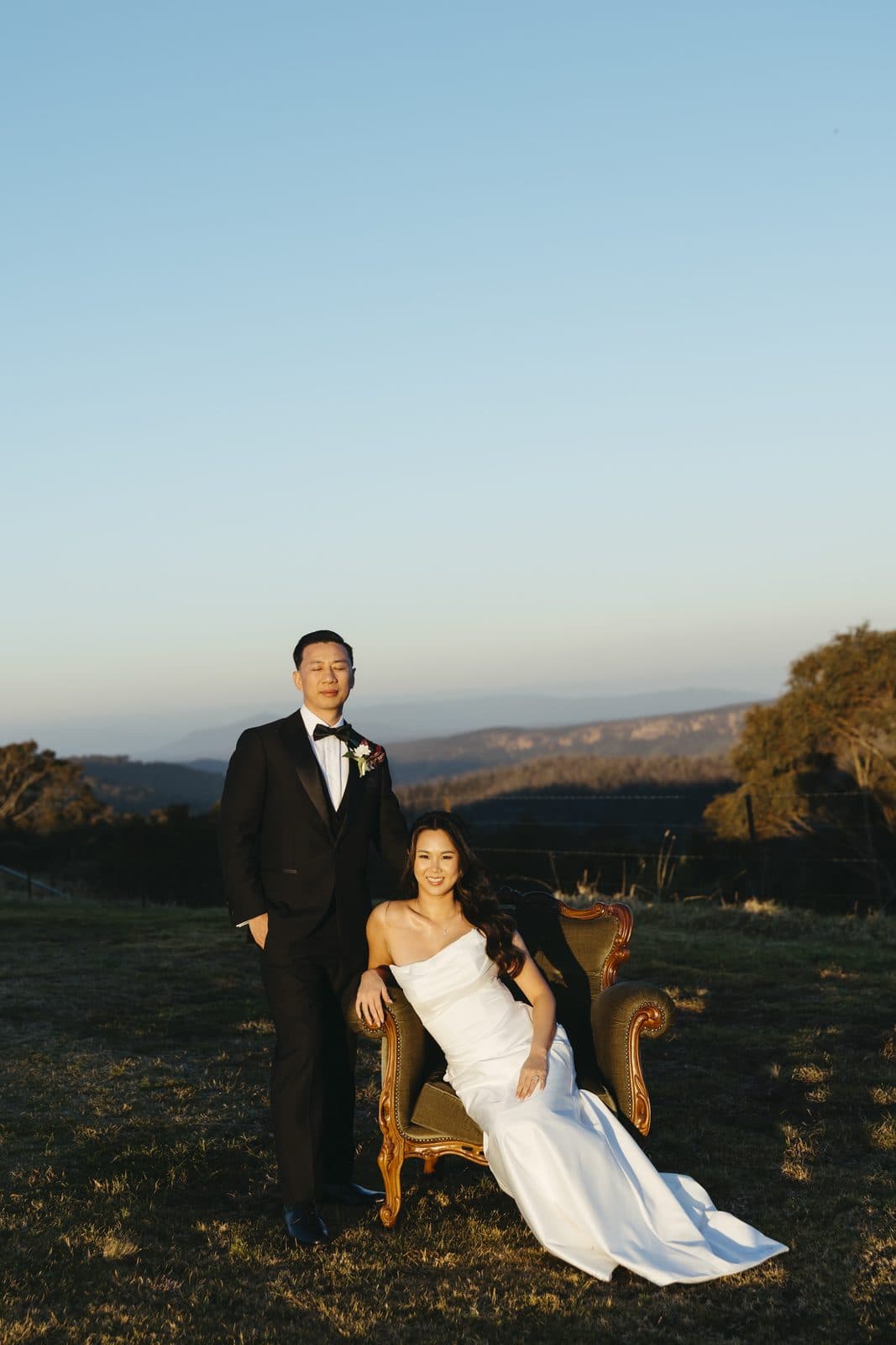 Ann seated in a green vintage armchair in the paddock, Winston standing beside her, the gorge and the far escarpment behind them in the last light