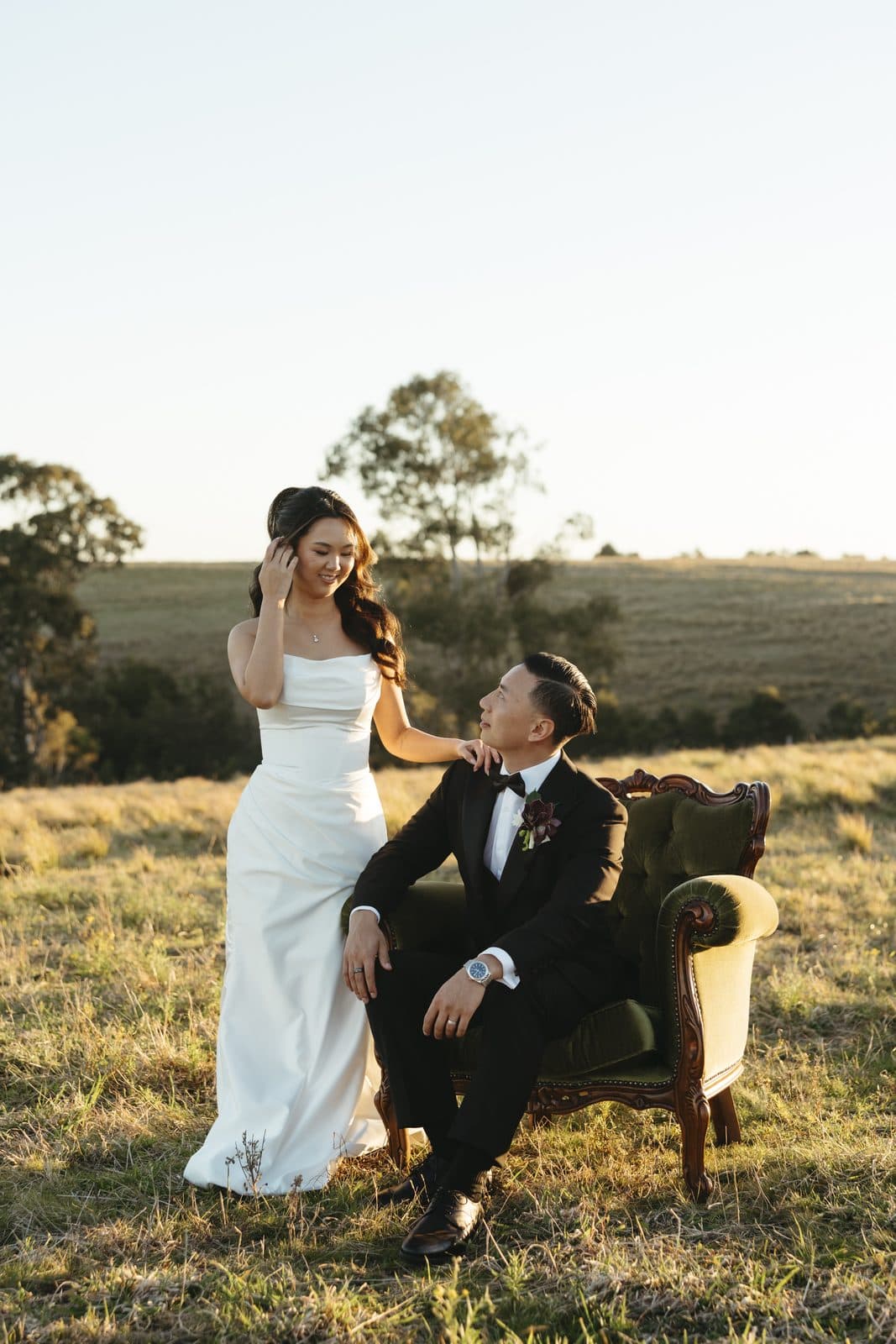 Ann and Winston in the paddock at golden hour, Winston seated in a green vintage armchair and Ann standing beside him