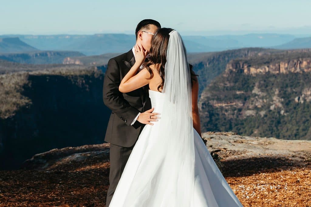 Ann and Winston kissing at the cliff edge, the gorge and the far escarpment behind them