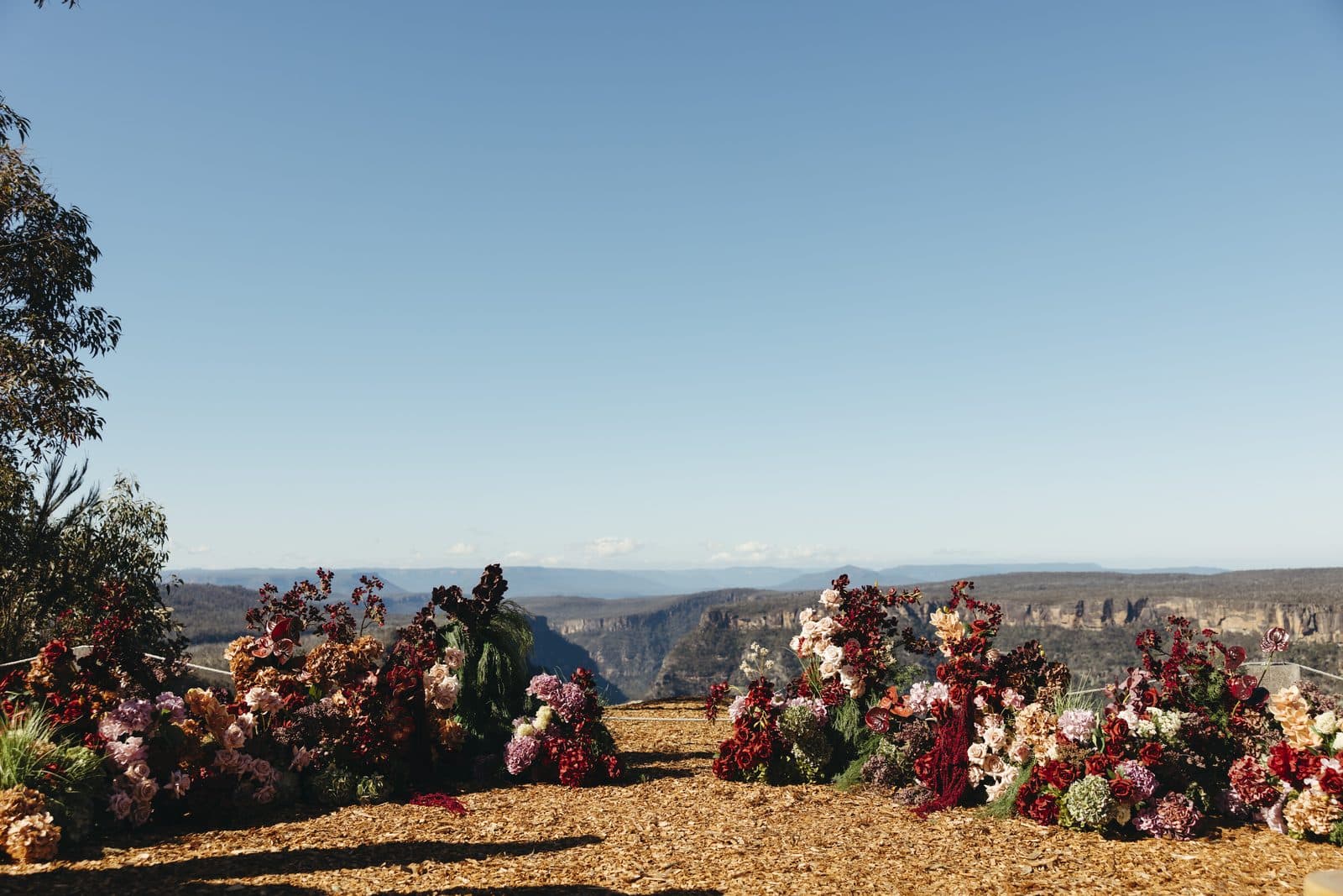 Deep red and pink florals either side of the ceremony spot at the cliff edge, the gorge running out behind