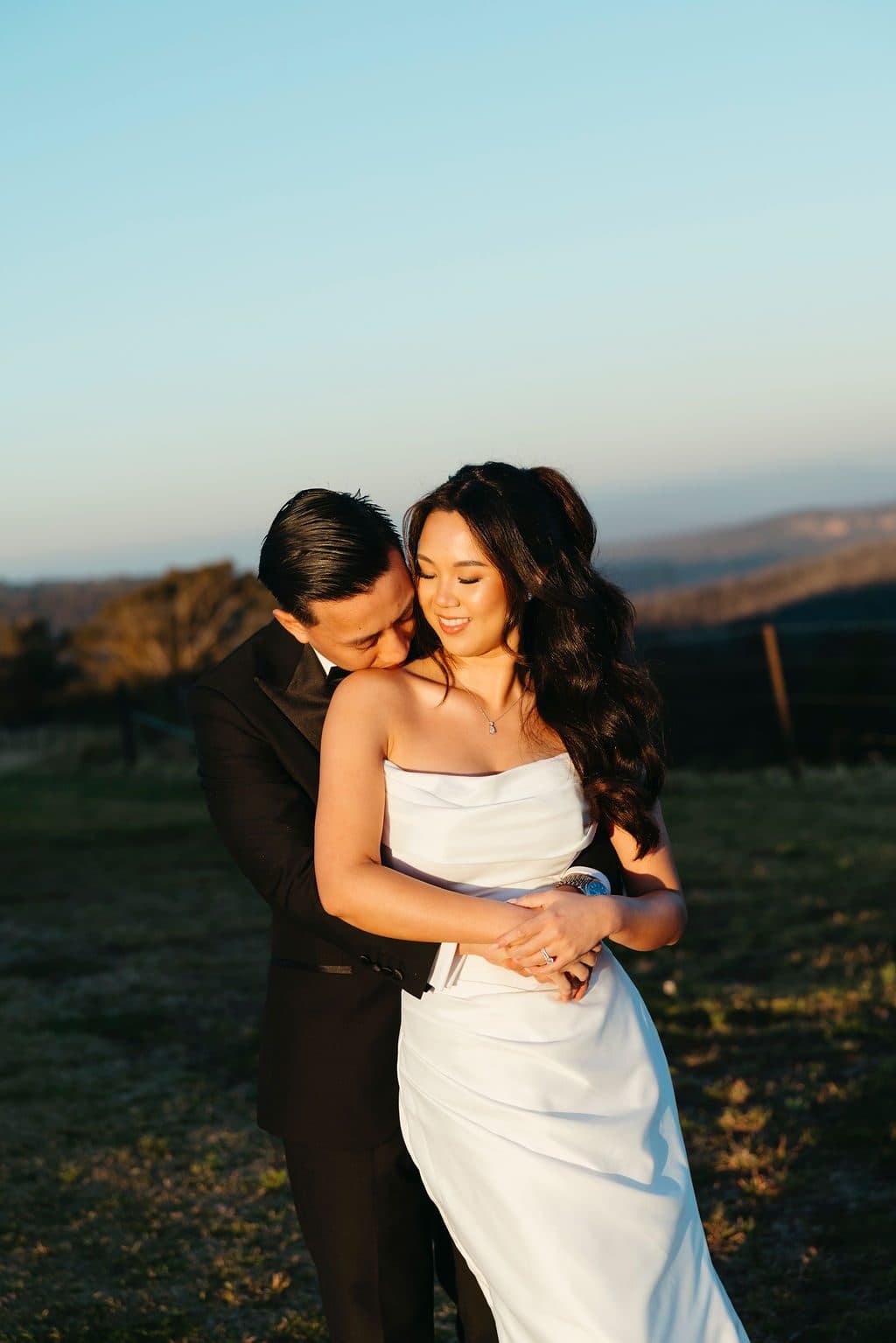 Winston holding Ann from behind in the last of the sun, the escarpment behind them