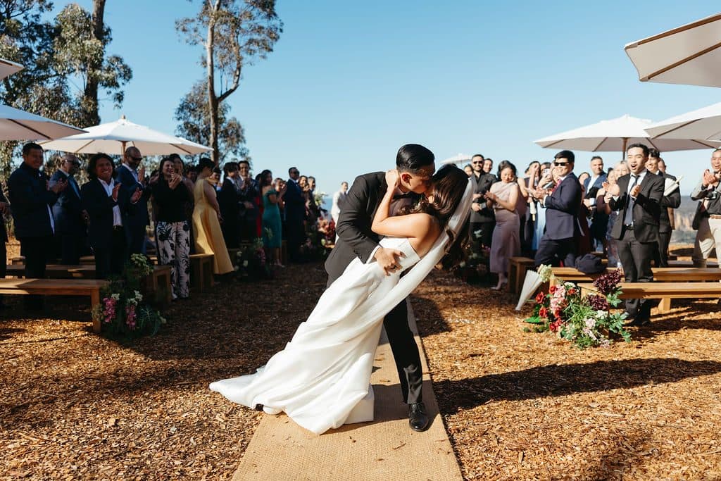 Winston dipping Ann into a kiss on the aisle as guests cheer from the benches