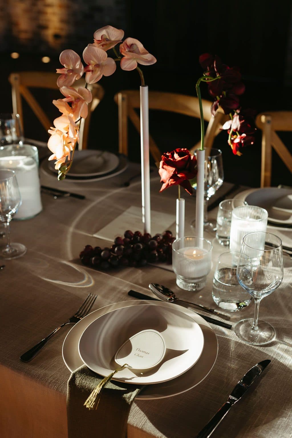 A place setting on the long table, orchids in bud vases and tall white tapers