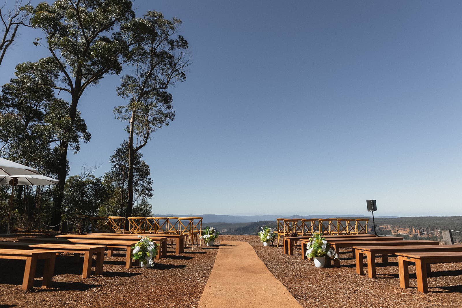 The clifftop ceremony site set with timber benches and a runner, the aisle drawing the eye toward the Shoalhaven gorge