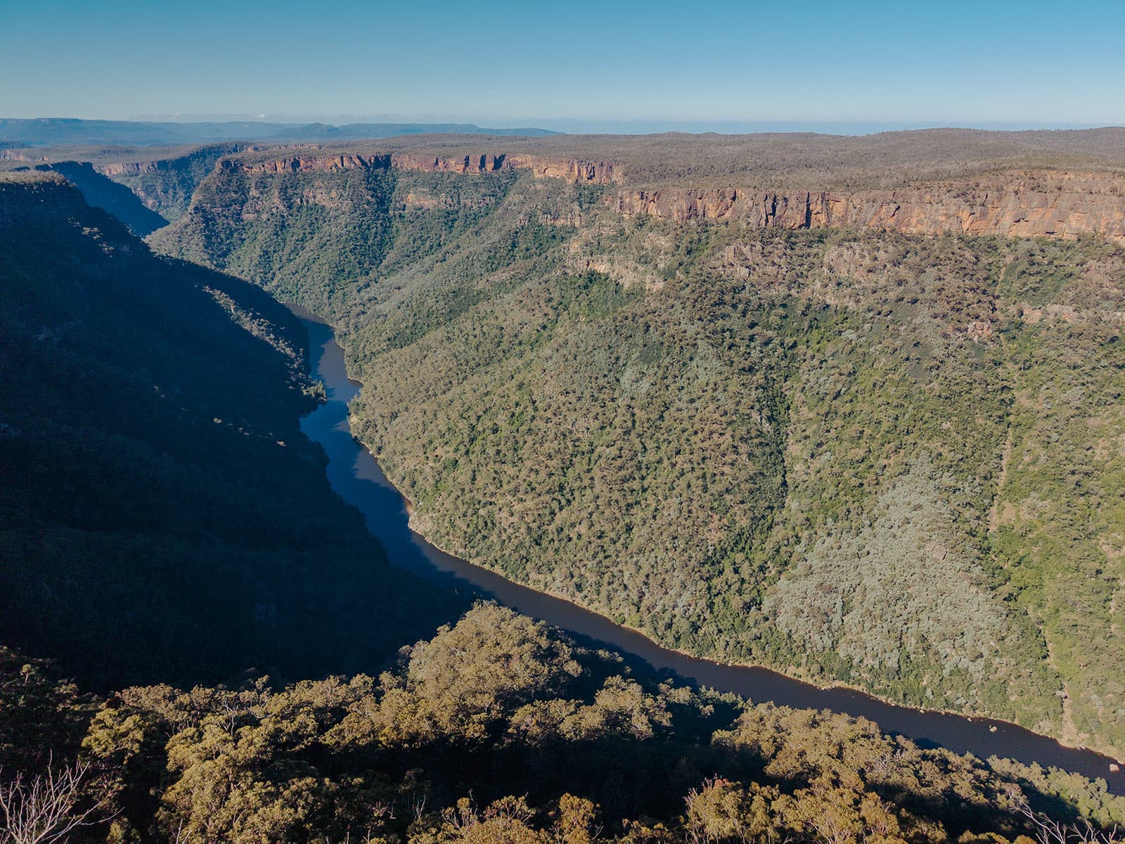 The Shoalhaven River carving through the gorge beneath the cliffs at Caoura, under a clear blue sky