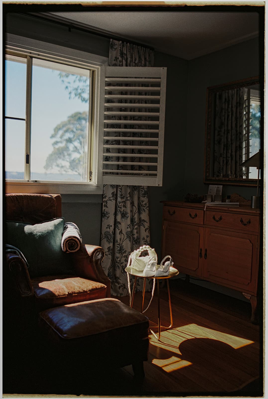 Morning light across a leather armchair and plantation shutters at The Homestead