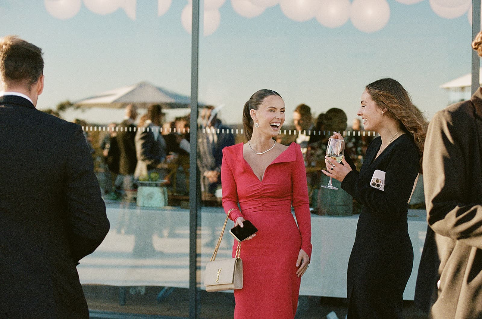 Guests talking over a glass at cocktail hour, the terrace and the escarpment through the Pavilion glass behind them