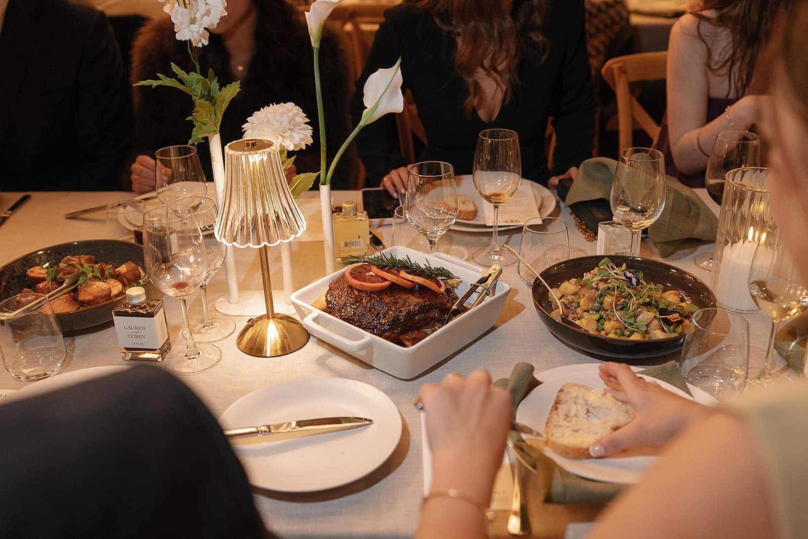 The long table at dinner under a small lamp, guests serving themselves from the shared dishes