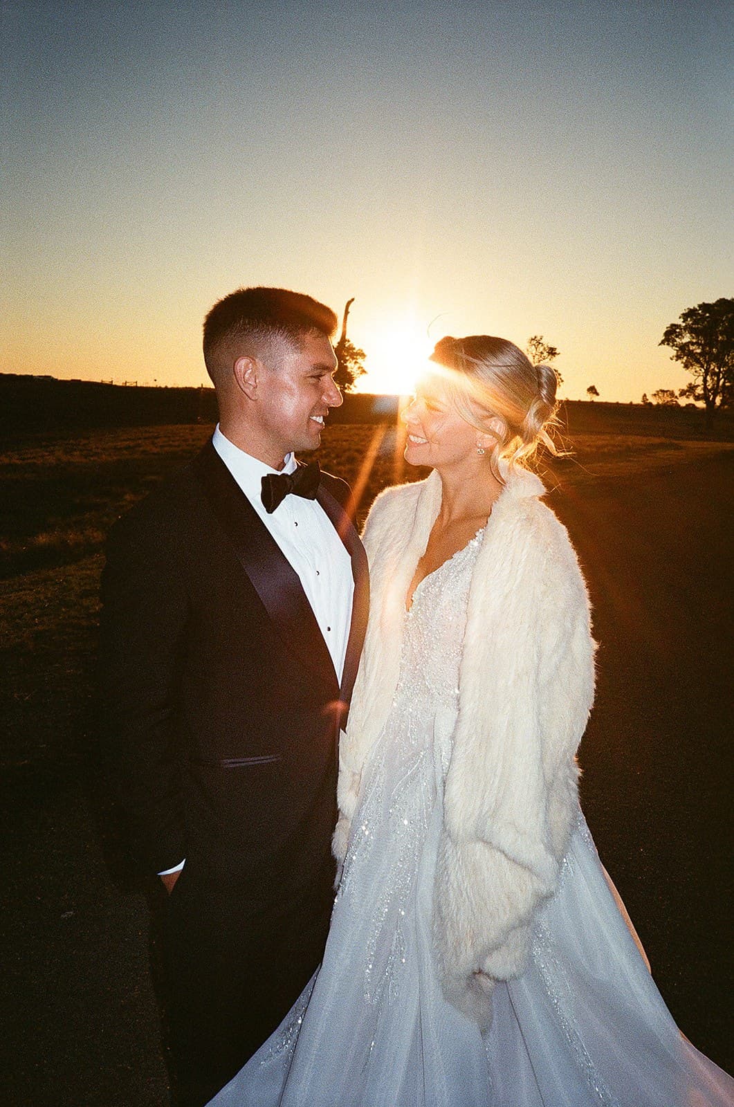 Lauren and Corey facing each other at sunset, the sun breaking between them over the ridge line