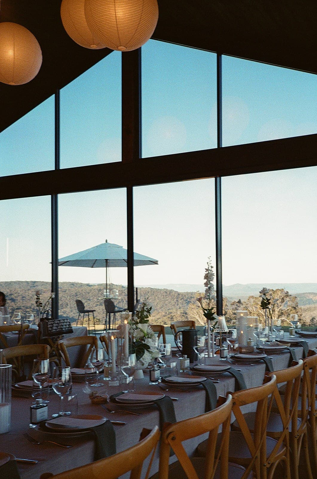 The Pavilion long tables set for dinner under the lanterns, the escarpment through the gabled glass