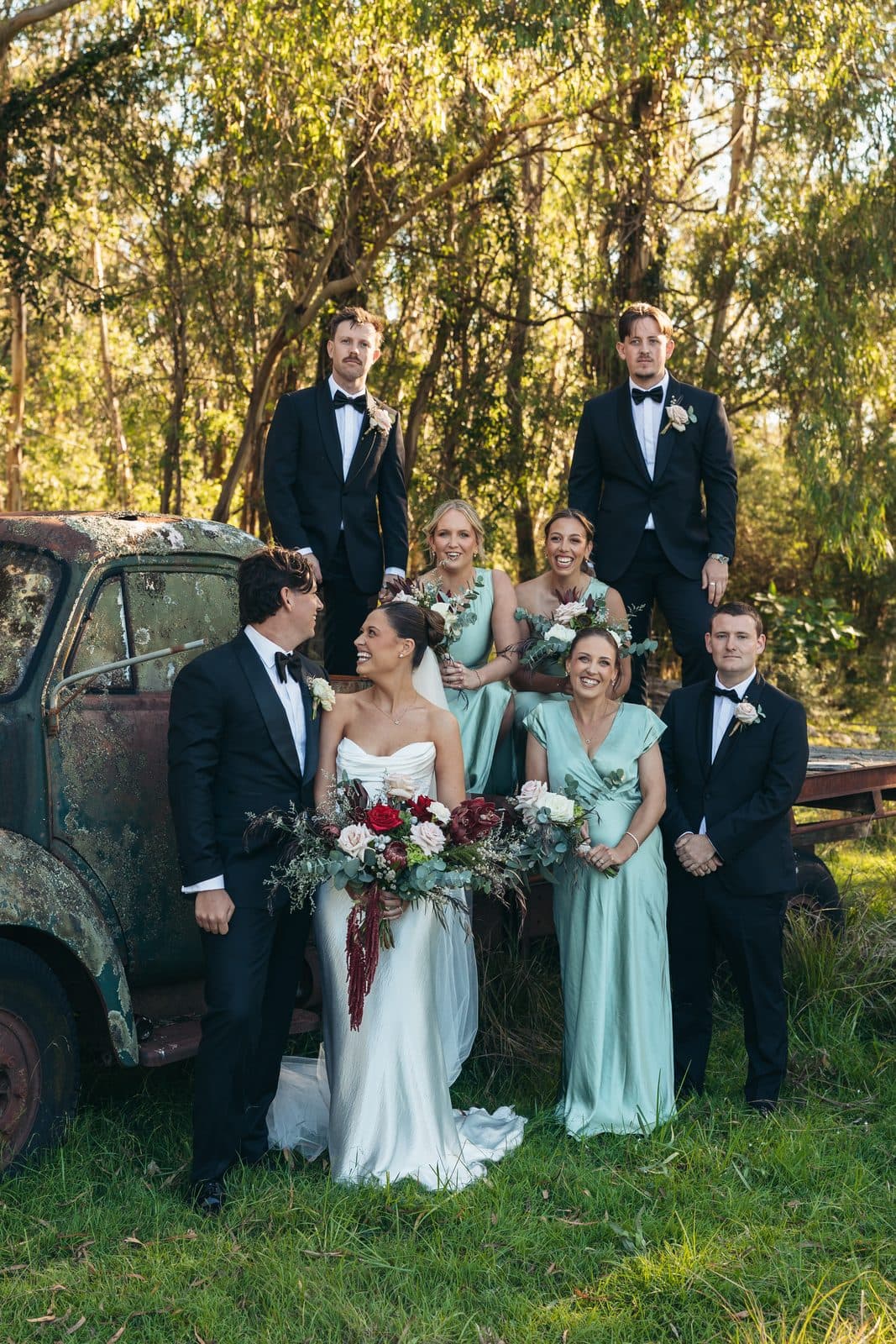 Liv and Ryan with the bridesmaids in sage green and the groomsmen, gathered beside an old farm truck in the gums