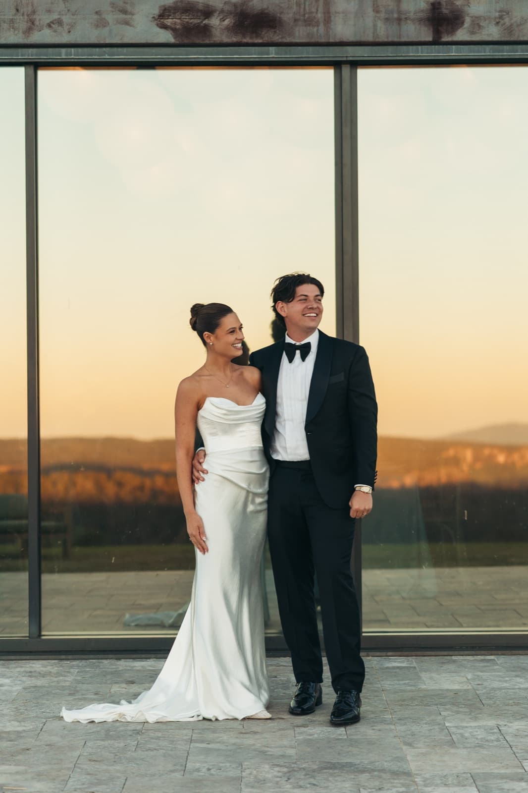 A bride and groom in front of the Pavilion's glass, the sunset reflected behind them