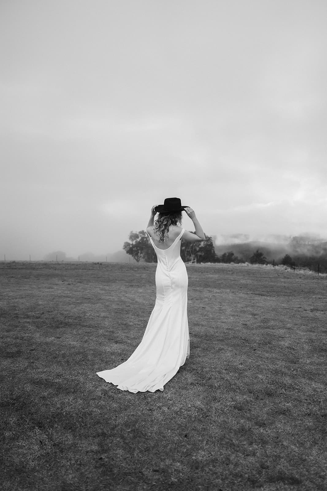 A bride in a Moira Hughes crepe gown and wide-brimmed hat looking out over the misted gorge