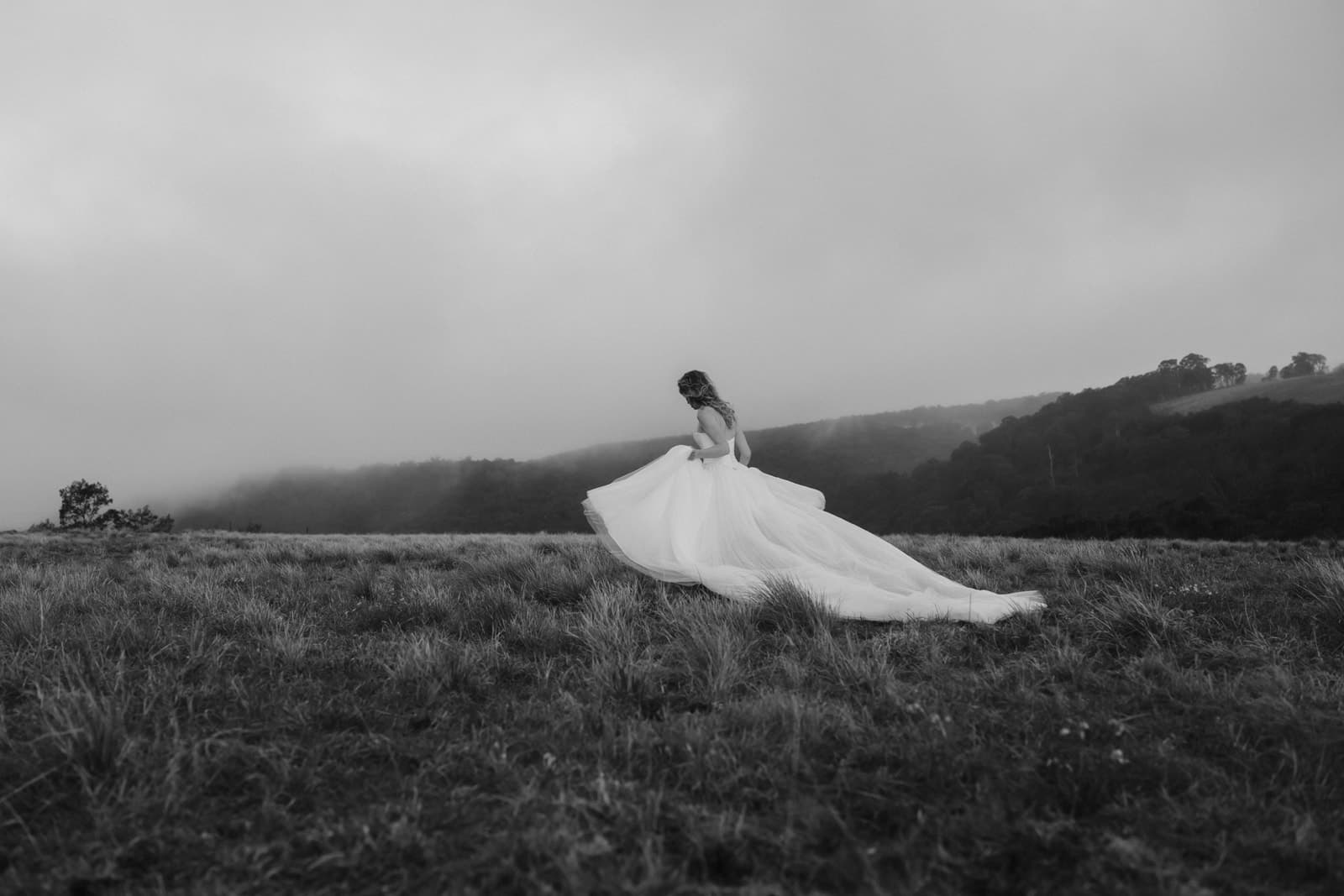 A bride in a tulle Moira Hughes gown crossing the hilltop as mist rolls over the Shoalhaven gorge