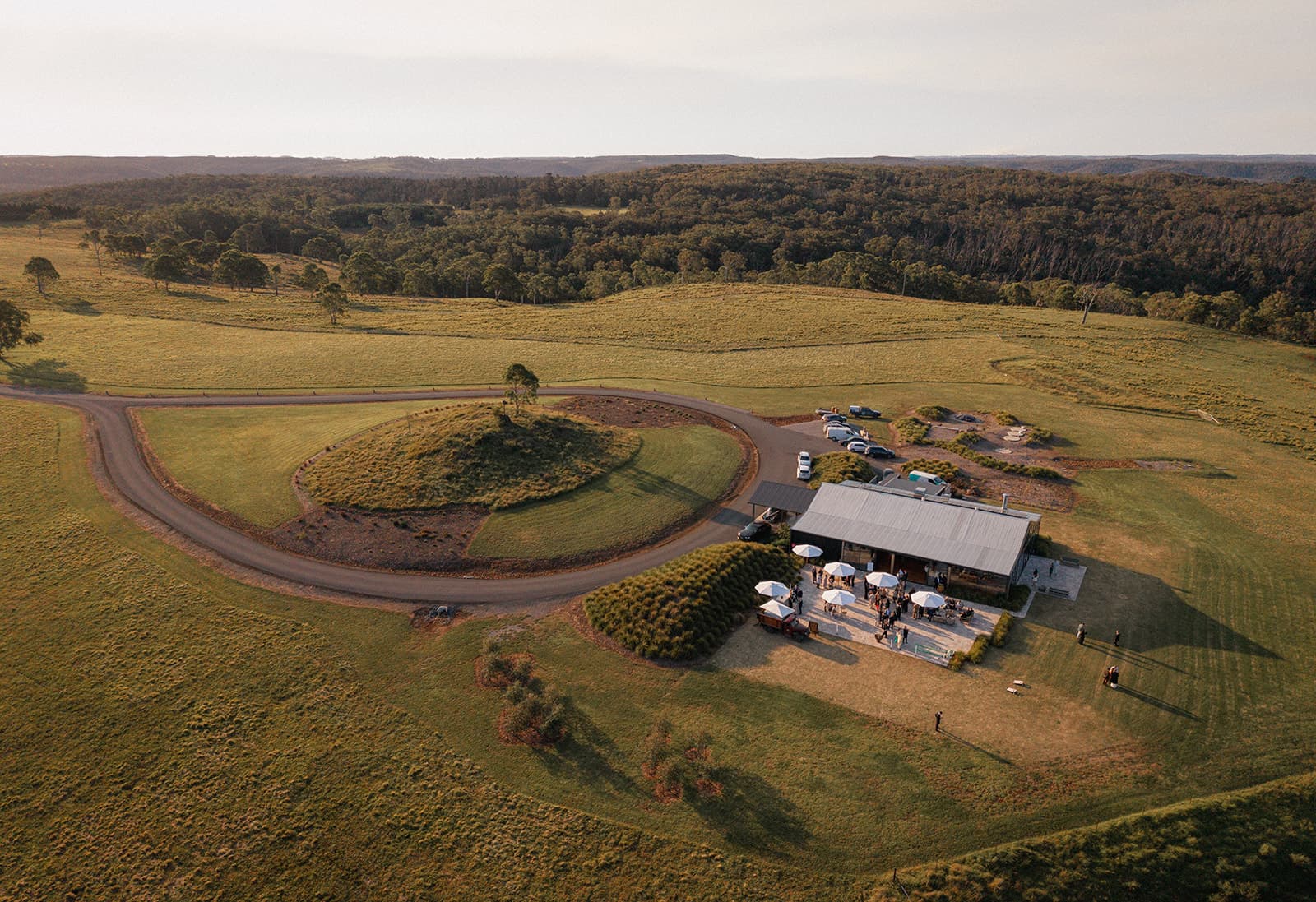 The glass Pavilion and its circular drive from the air at golden hour, the escarpment rolling away beyond