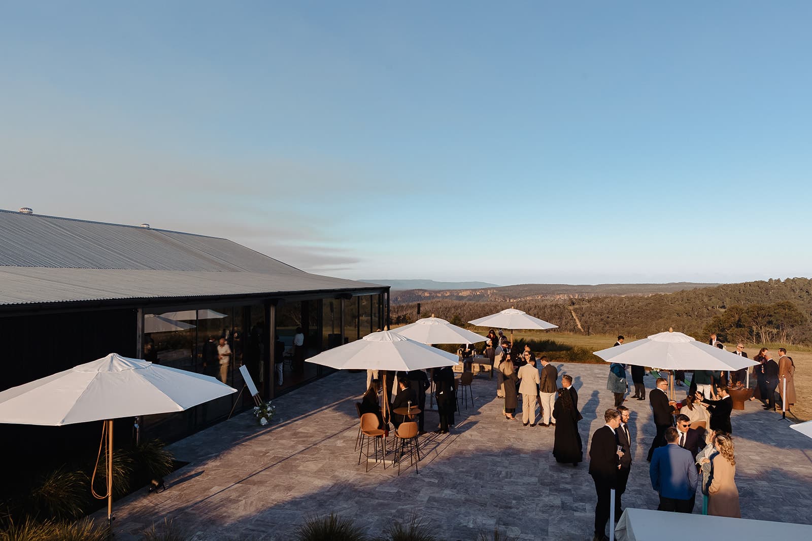 Golden hour on the Pavilion terrace, guests gathered under white umbrellas above the gorge