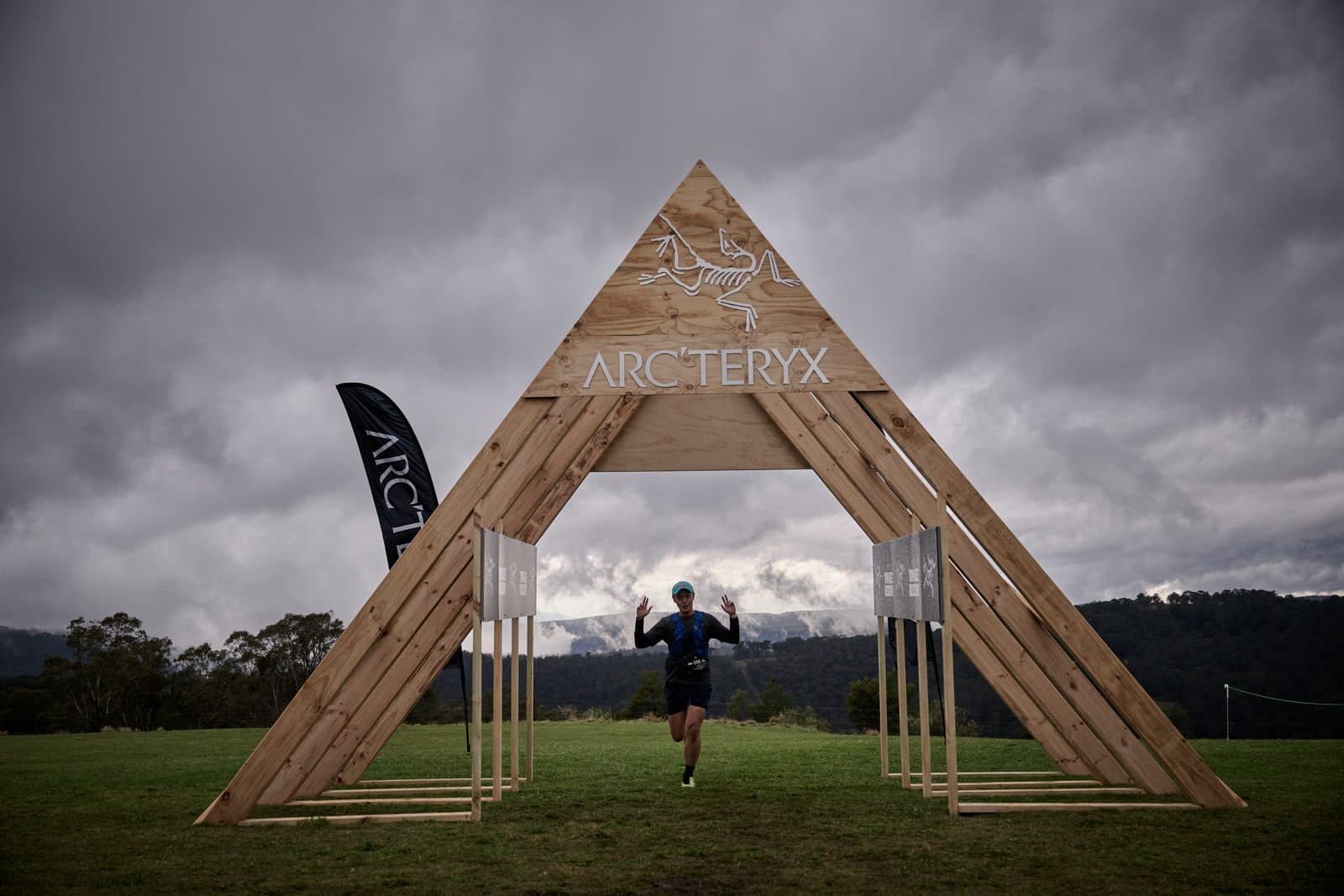 A runner coming through the timber arch to the finish under a storm sky, cloud sitting in the gorge behind