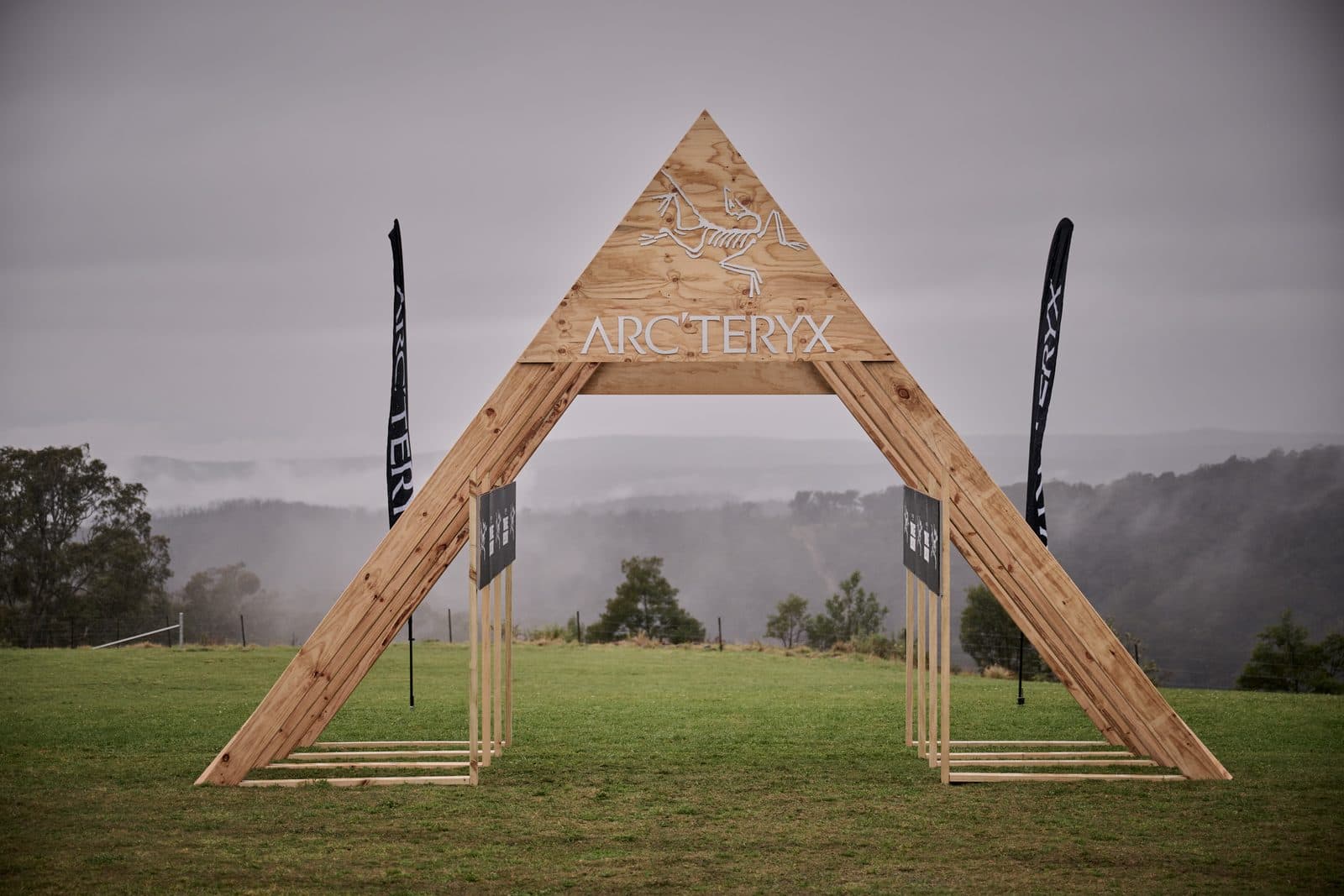 The timber Arc'teryx arch standing empty on the lawn before the start, fog lifting off the gorge behind
