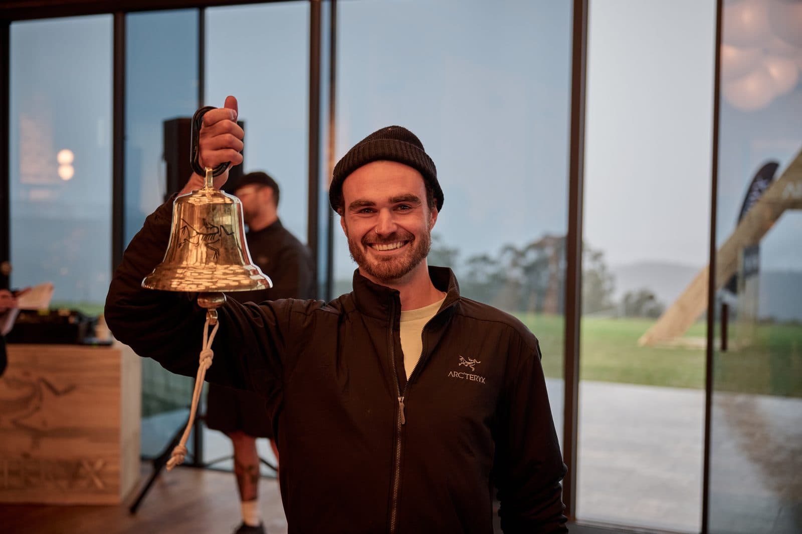 A runner holding up the brass bell inside the Pavilion, the glass and the ranges behind