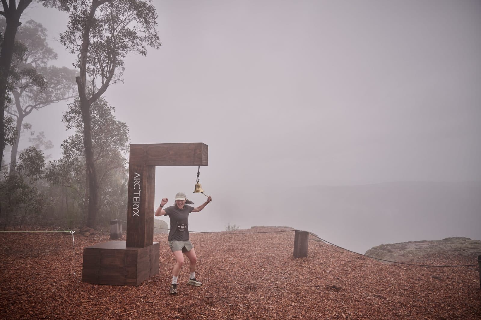 A runner reaching for the bell at the edge, fog where the gorge should be