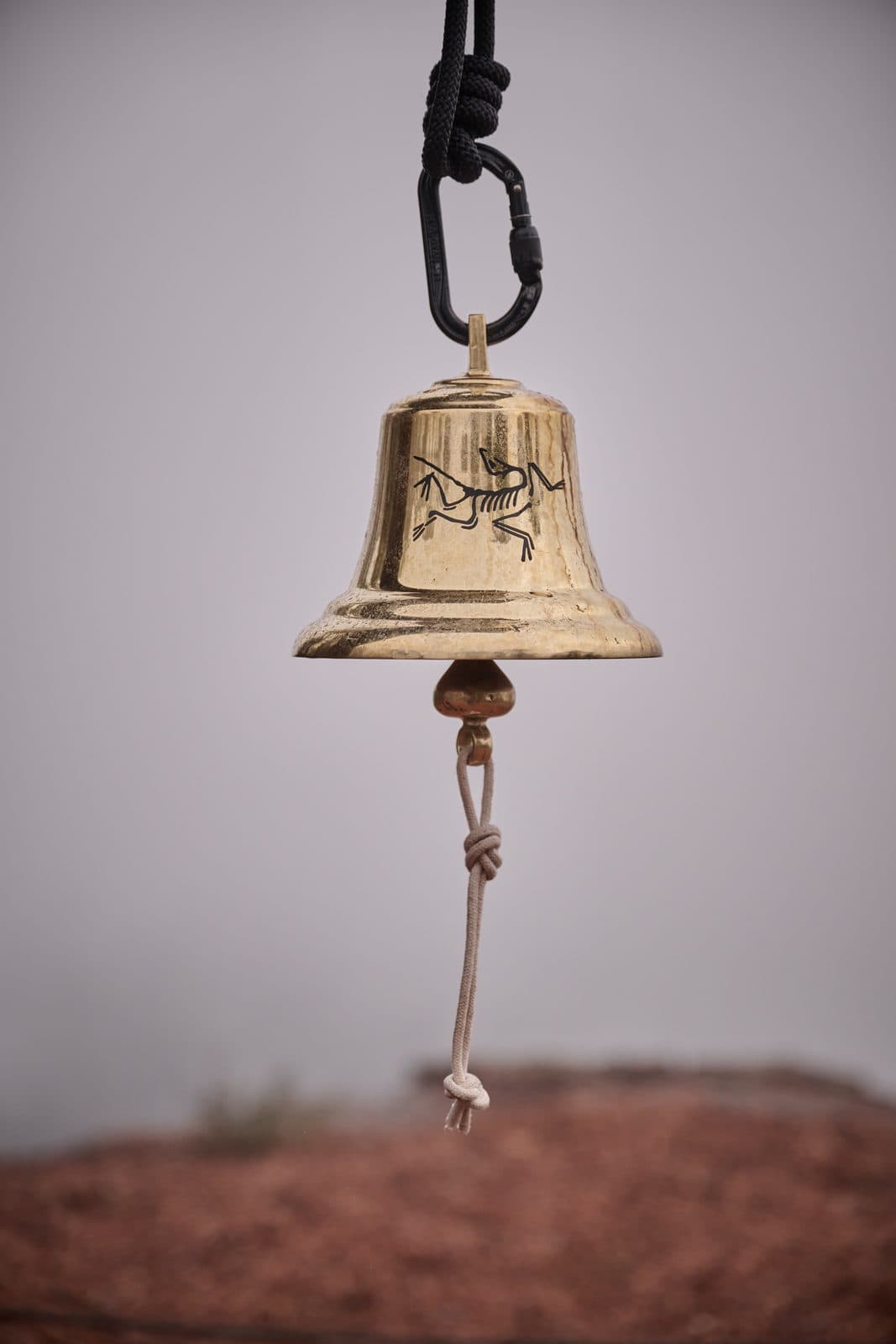 The brass bell against white fog, the Arc'teryx bird on its side