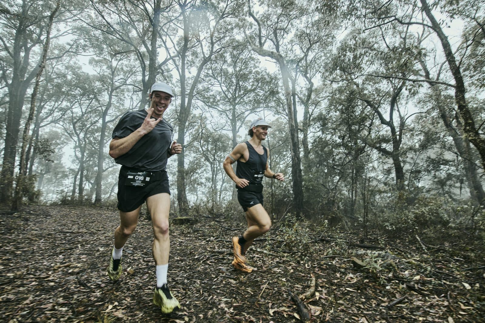 Two runners coming through misty bush over a carpet of leaf litter