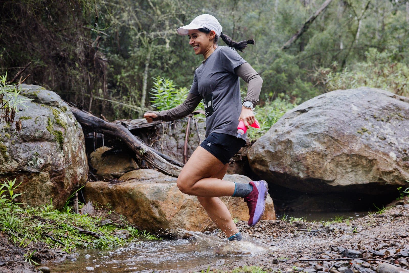 A runner stepping between boulders at the creek, ferns and gums around her