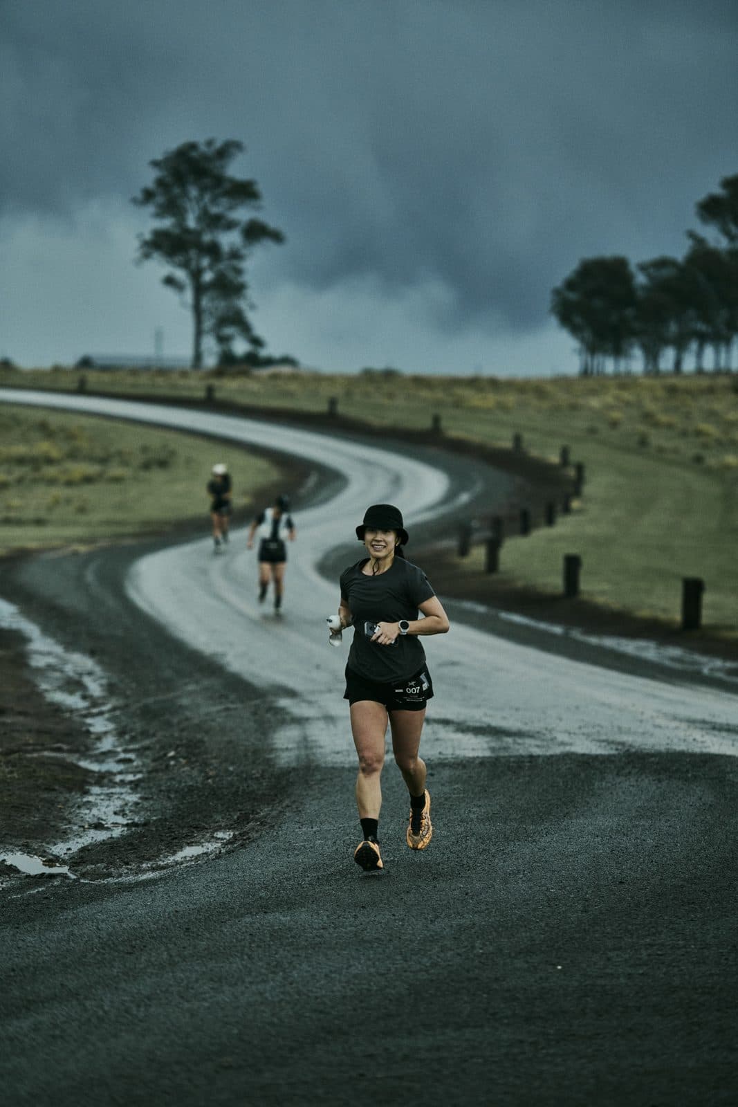 A runner on the wet farm road as it curves away through open paddock under heavy cloud