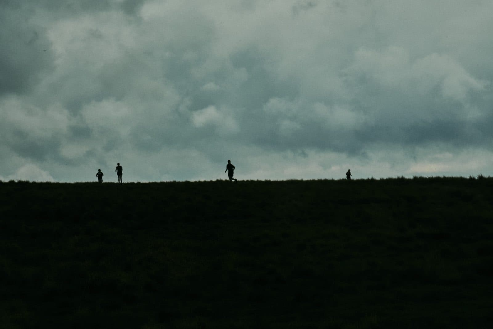 Three runners in silhouette on the crest of a paddock under a grey sky