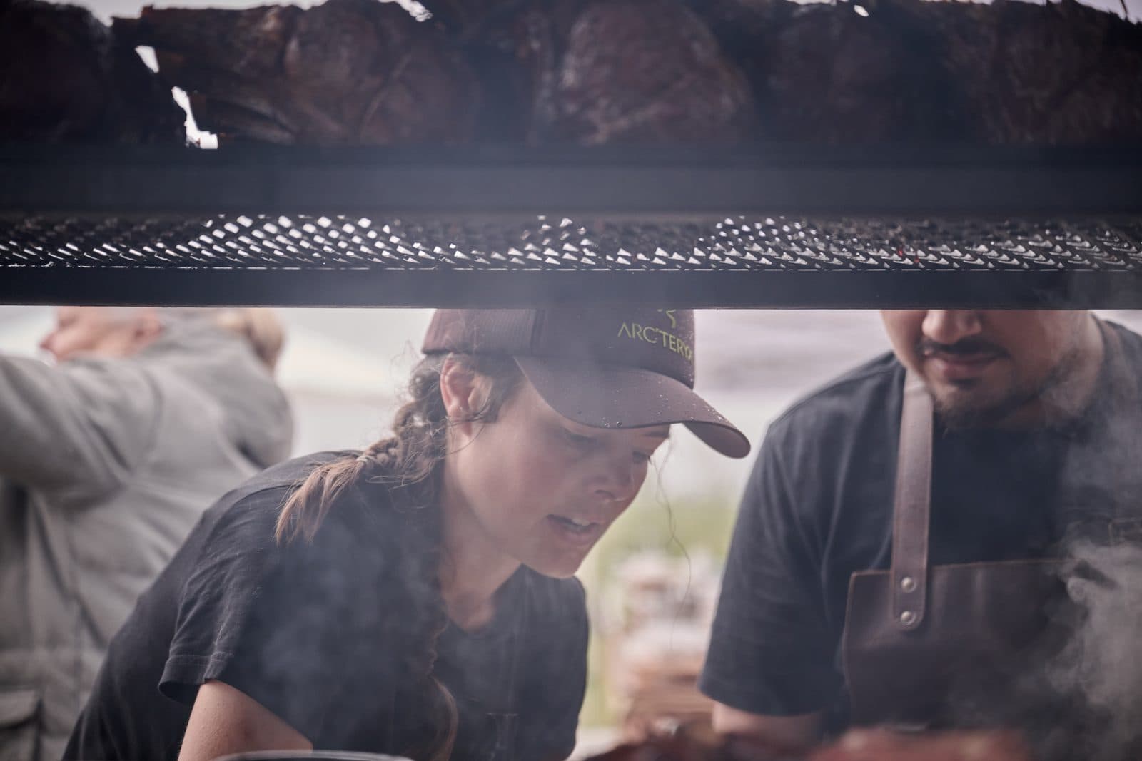 Two chefs working in smoke under a grill rack