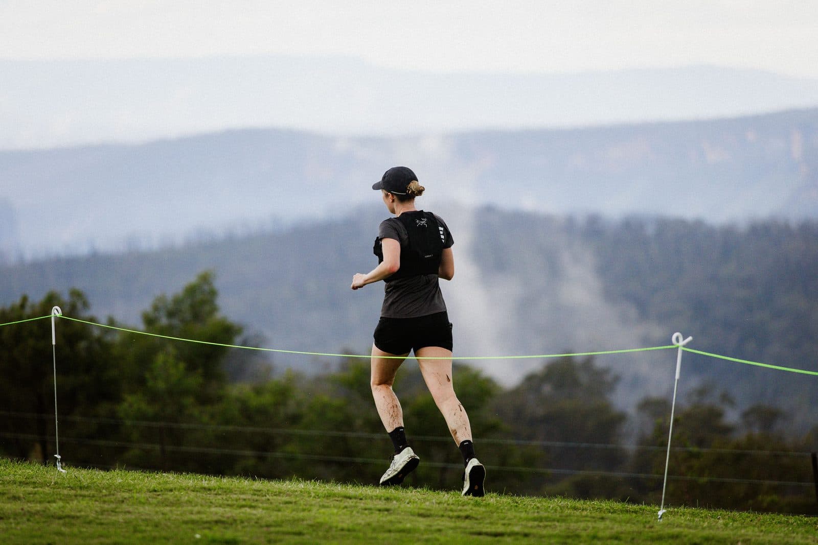 A runner crossing the lawn at Caoura Cliffs, mist rising out of the gorge below the ranges