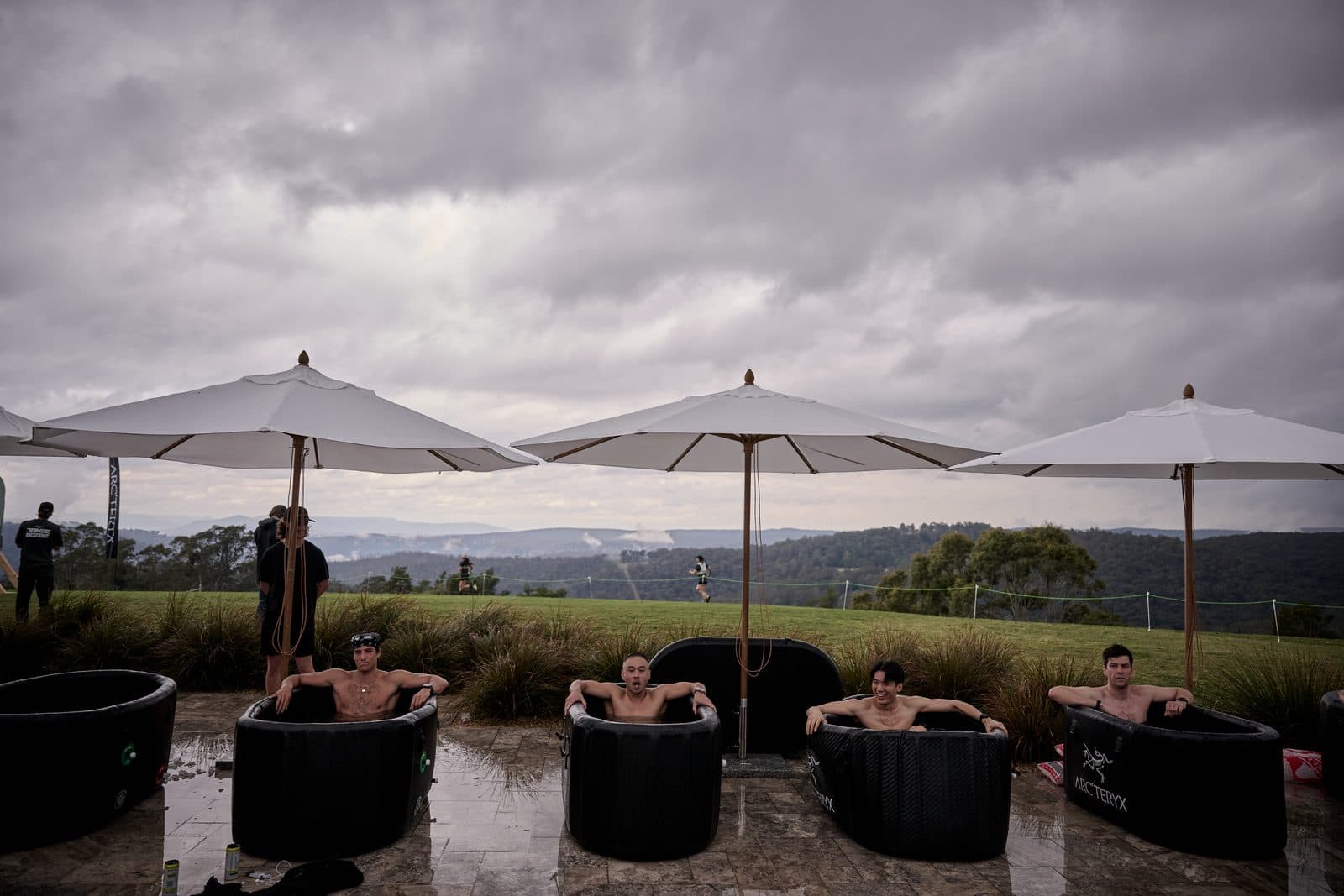 A row of ice baths under white umbrellas on the terrace, the ranges and low cloud beyond