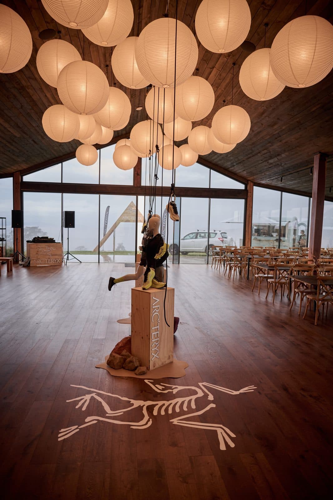 Paper lanterns above the Pavilion floor, the Arc'teryx bird projected onto the floorboards beneath a single plinth