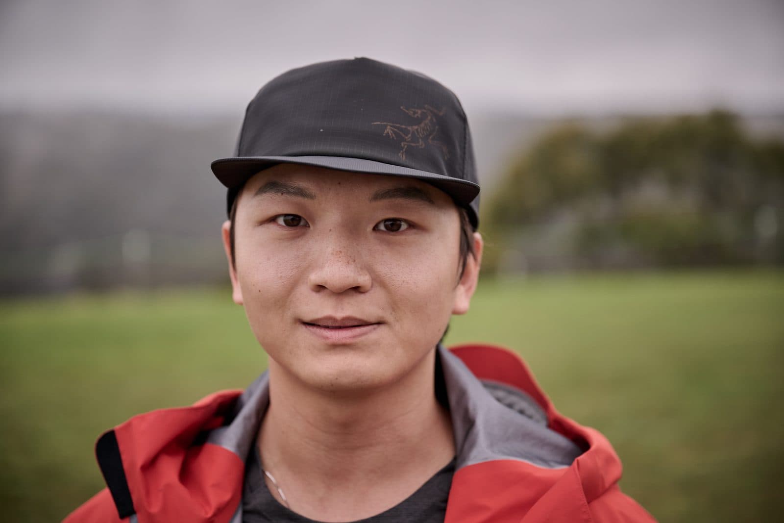 A runner in a black cap and red jacket, mist on the treeline behind