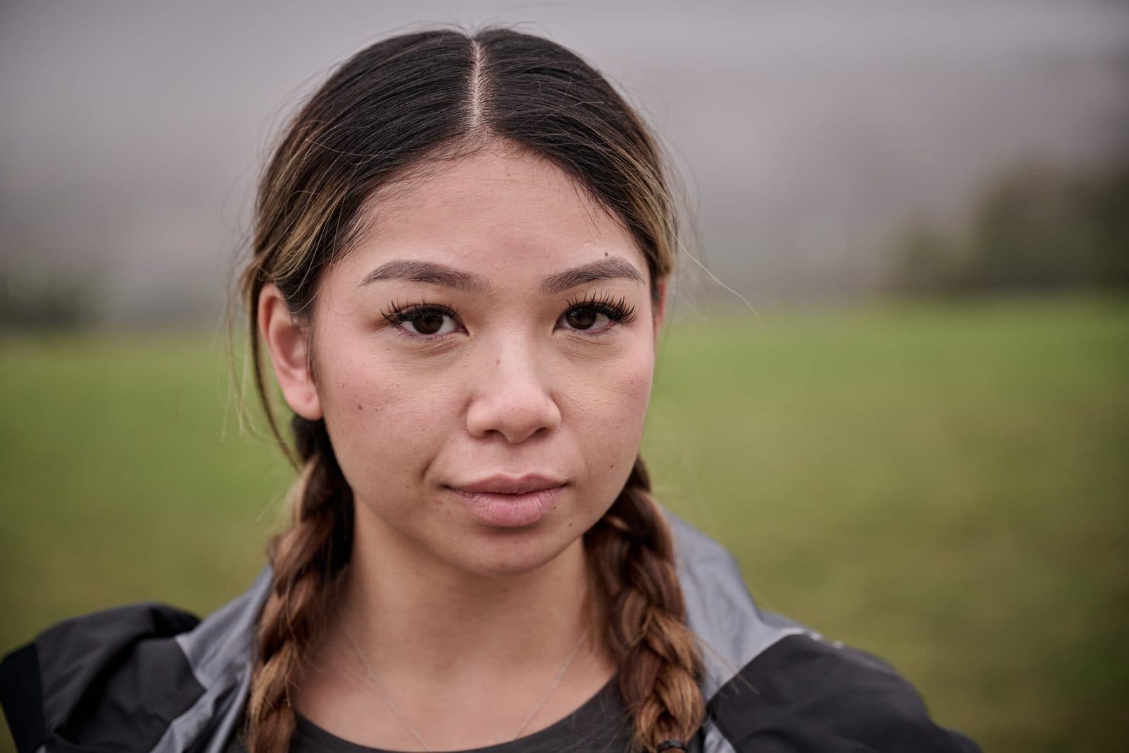 A runner with two long braids looking into the camera, the lawn soft behind her