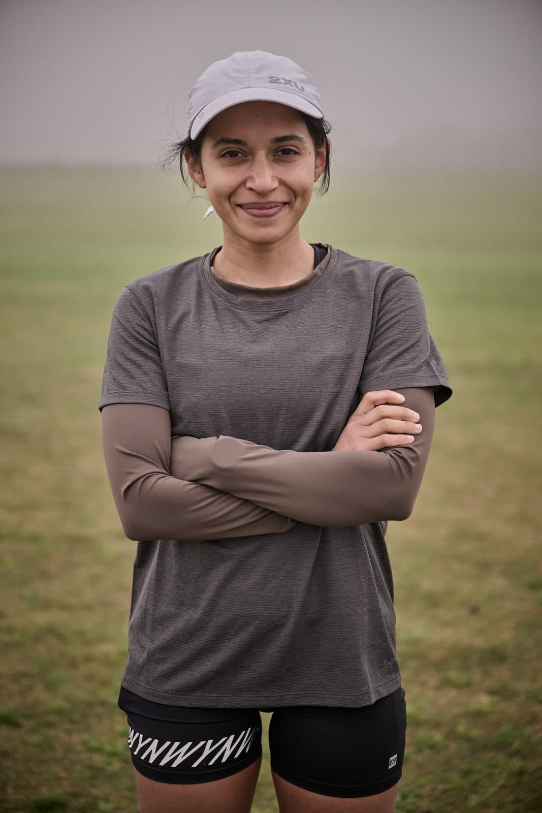 A runner with folded arms in a grey cap, the paddock and fog behind