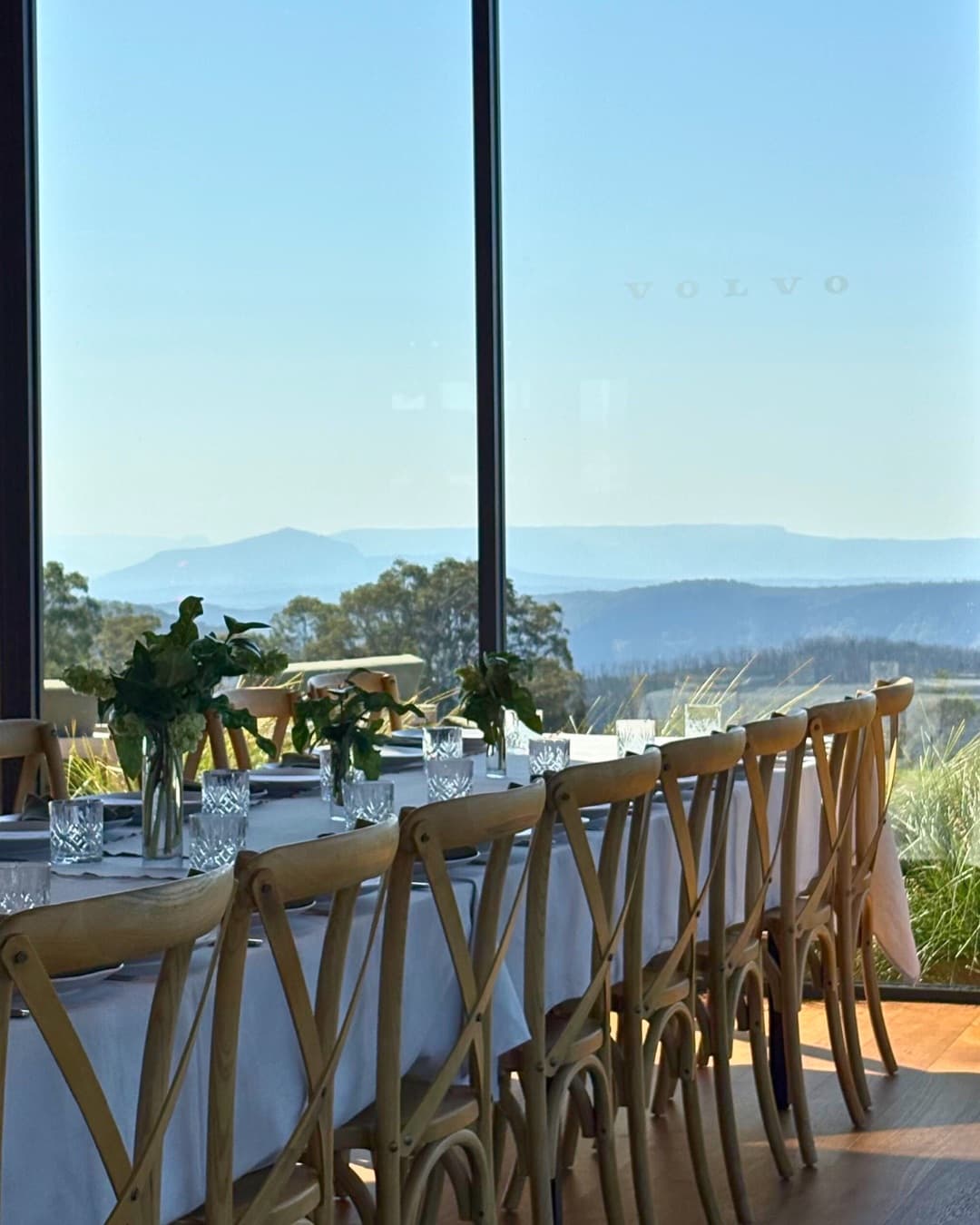 The Pavilion set for a seated dinner, the VOLVO wordmark across the floor-to-ceiling glass and the vehicle range lined up outside