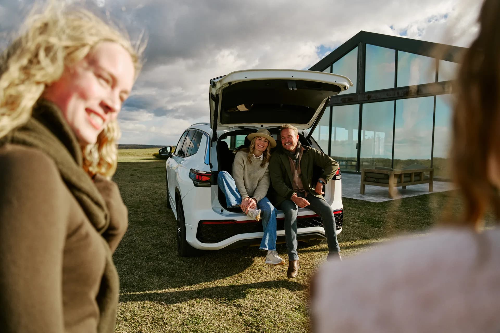 A couple sitting in the open boot of the Volkswagen Tayron on the lawn, the Pavilion glass behind them