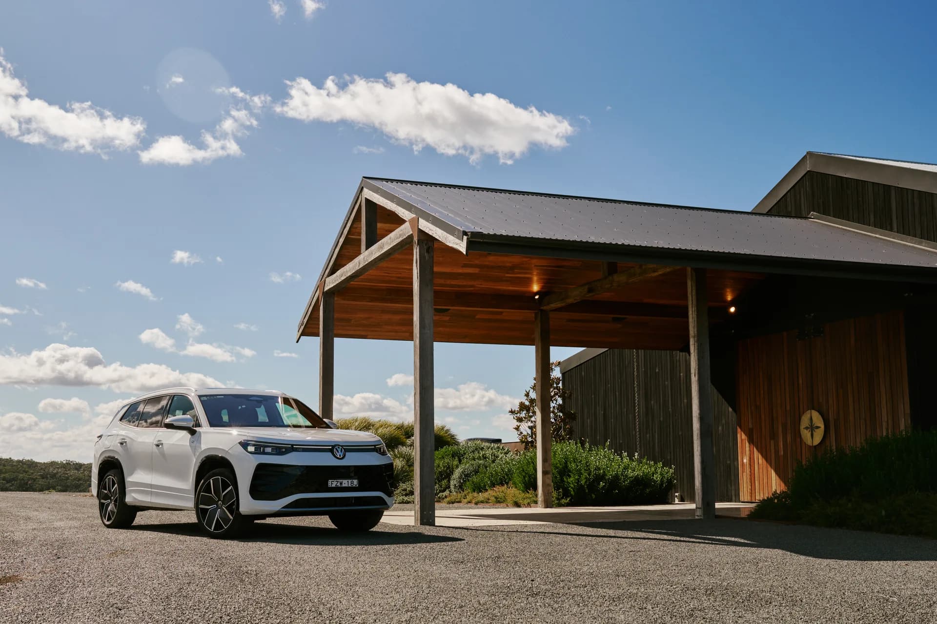 A white Volkswagen Tayron parked on the gravel beside the timber carport at Caoura Cliffs, under an open blue sky