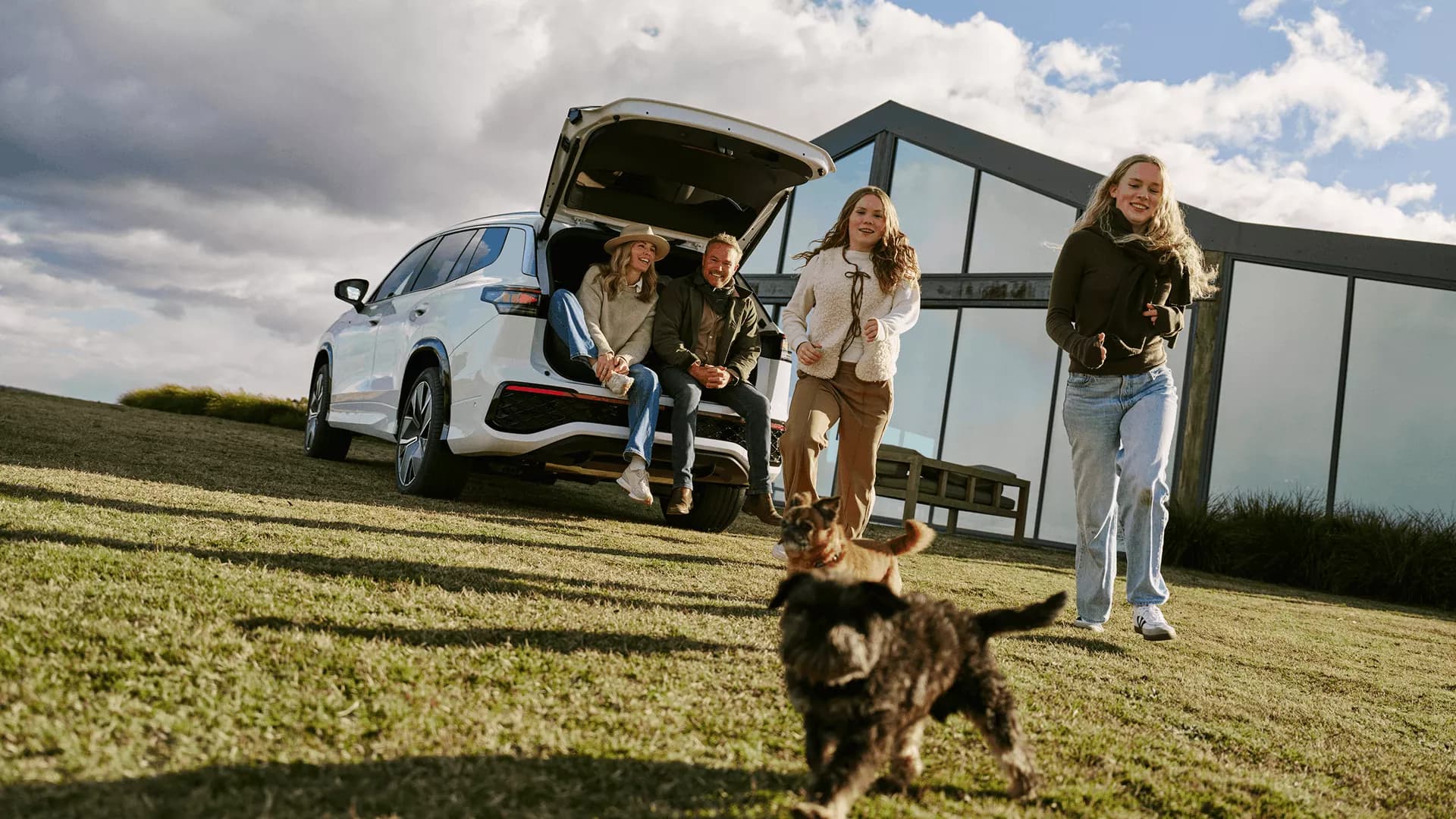 A family and their dogs at the open boot of a Volkswagen Tayron, in front of the Pavilion glass at Caoura Cliffs
