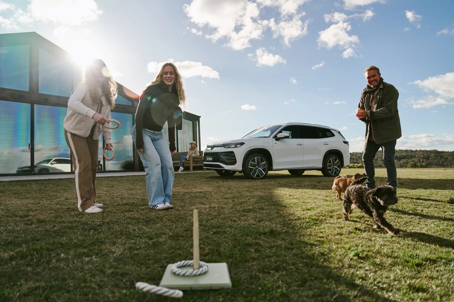 A family playing quoits on the lawn beside the Pavilion, the Volkswagen Tayron parked behind them and two dogs running through the frame
