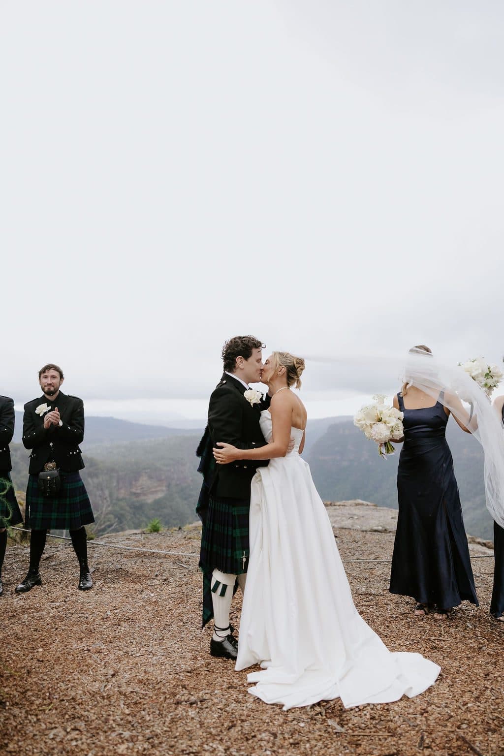 Anna and Calum's first kiss at the end of the aisle, the bridesmaids beside them and the gorge behind