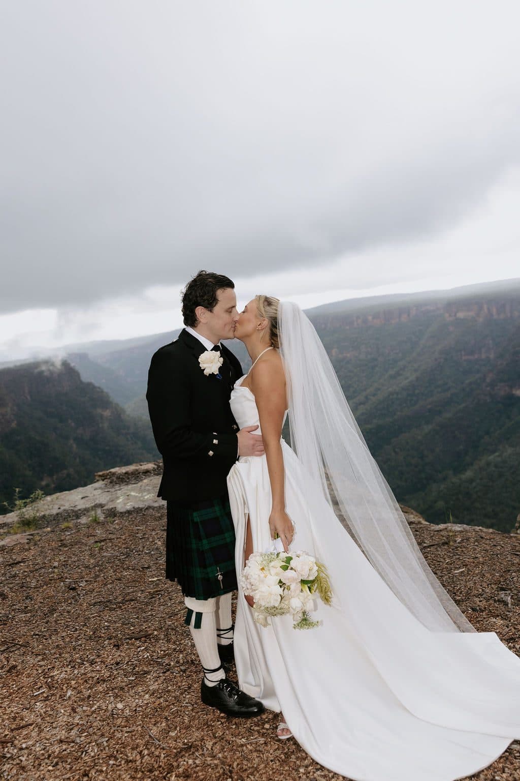 Anna and Calum kissing at the edge of The Cliffs, cloud pouring over the far escarpment