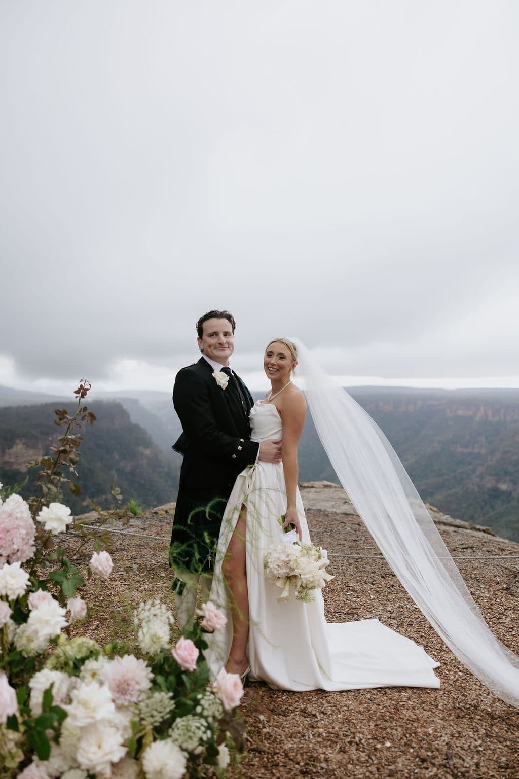 Anna and Calum at The Cliffs beside the ceremony florals, her veil blowing out over the gorge