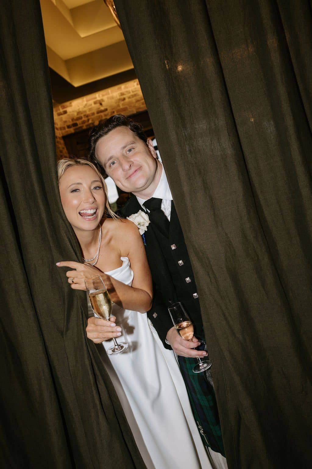 Anna and Calum stepping through the curtains into The Pavilion, glasses in hand