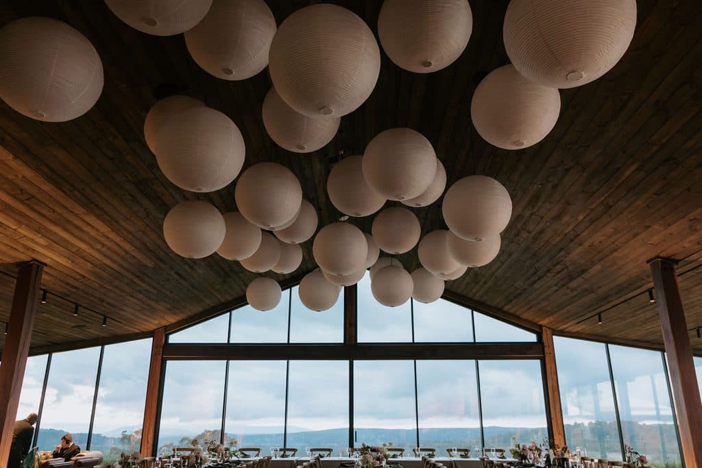 The Pavilion before dinner, paper lanterns hung under the timber ceiling and the escarpment through the gable glass