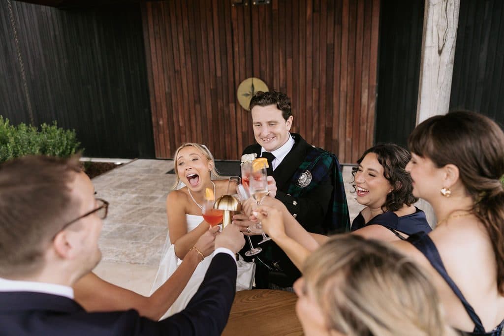 Anna and Calum laughing with friends at cocktail hour, drinks raised