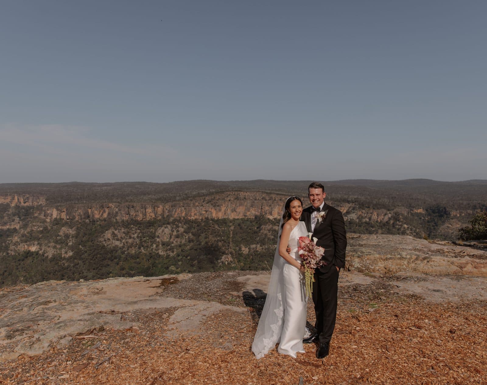 Jamae and Ben standing on the bare sandstone at the edge of The Cliffs, the gorge and the far escarpment behind them