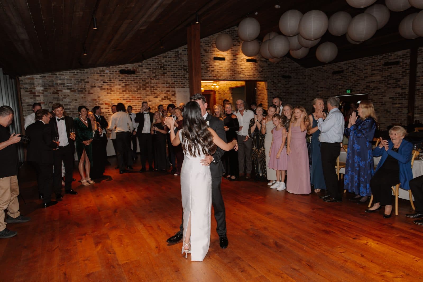 Jamae and Ben's first dance under the paper lanterns, guests standing around the floor