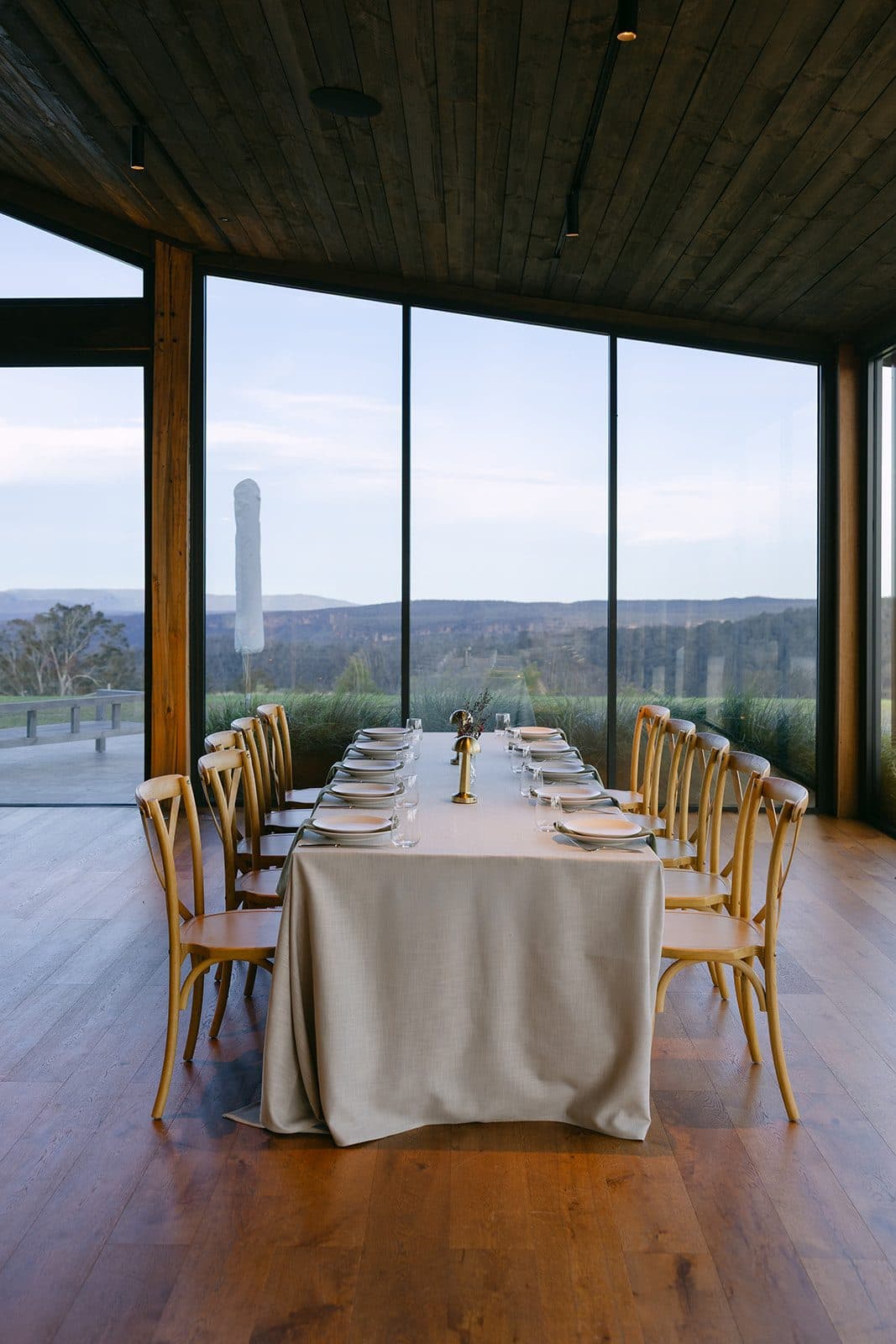One long table set for dinner in the Pavilion, the gorge and the ranges through the glass behind it